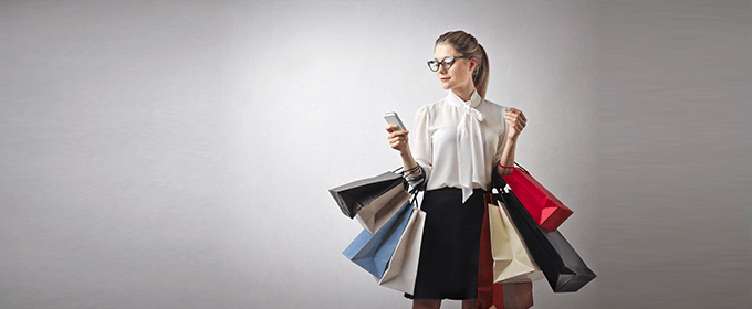 A woman carrying several shopping bags is looking at her smartphone.