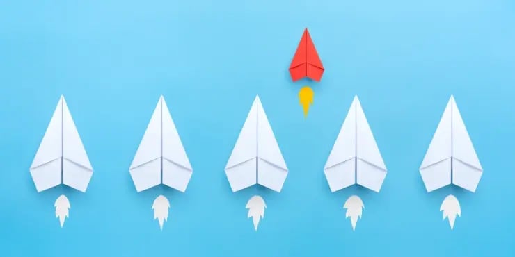red paper airplane separating from group of white ones