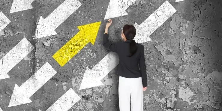 a woman drawing one yellow arrow going in the other direction from many white arrows
