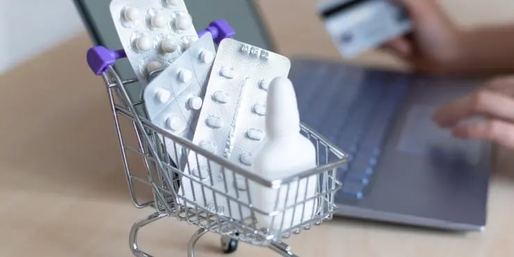 mini shopping cart filled with medicine with a laptop in the background