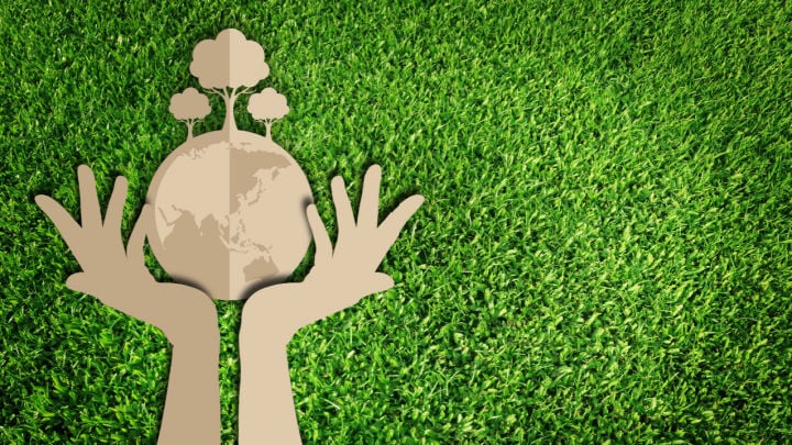 paper cut out of the hands holding planet on grass