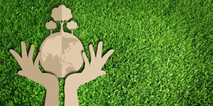 cardboard hands holding a cardboard earth on top of real grass