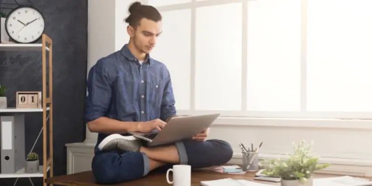 man doing yoga pose on his desk while using laptop