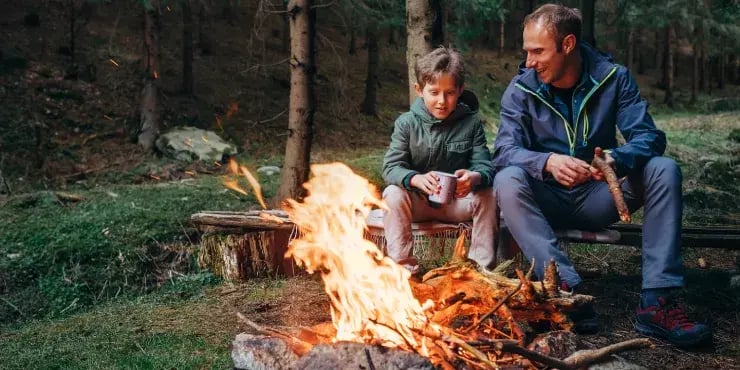 father and son sit around a campfire