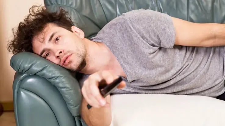 A lazy man on the couch watching TV.