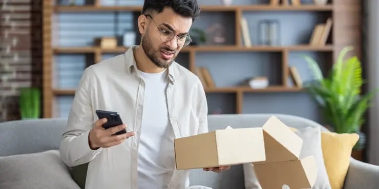 Unhappy man opening a package and on his phone.